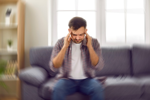 A man sitting on a sofa with a blurred, dizzying visual effect, holding his hands to his temples to depict a severe headache after a fall accident in Toronto.