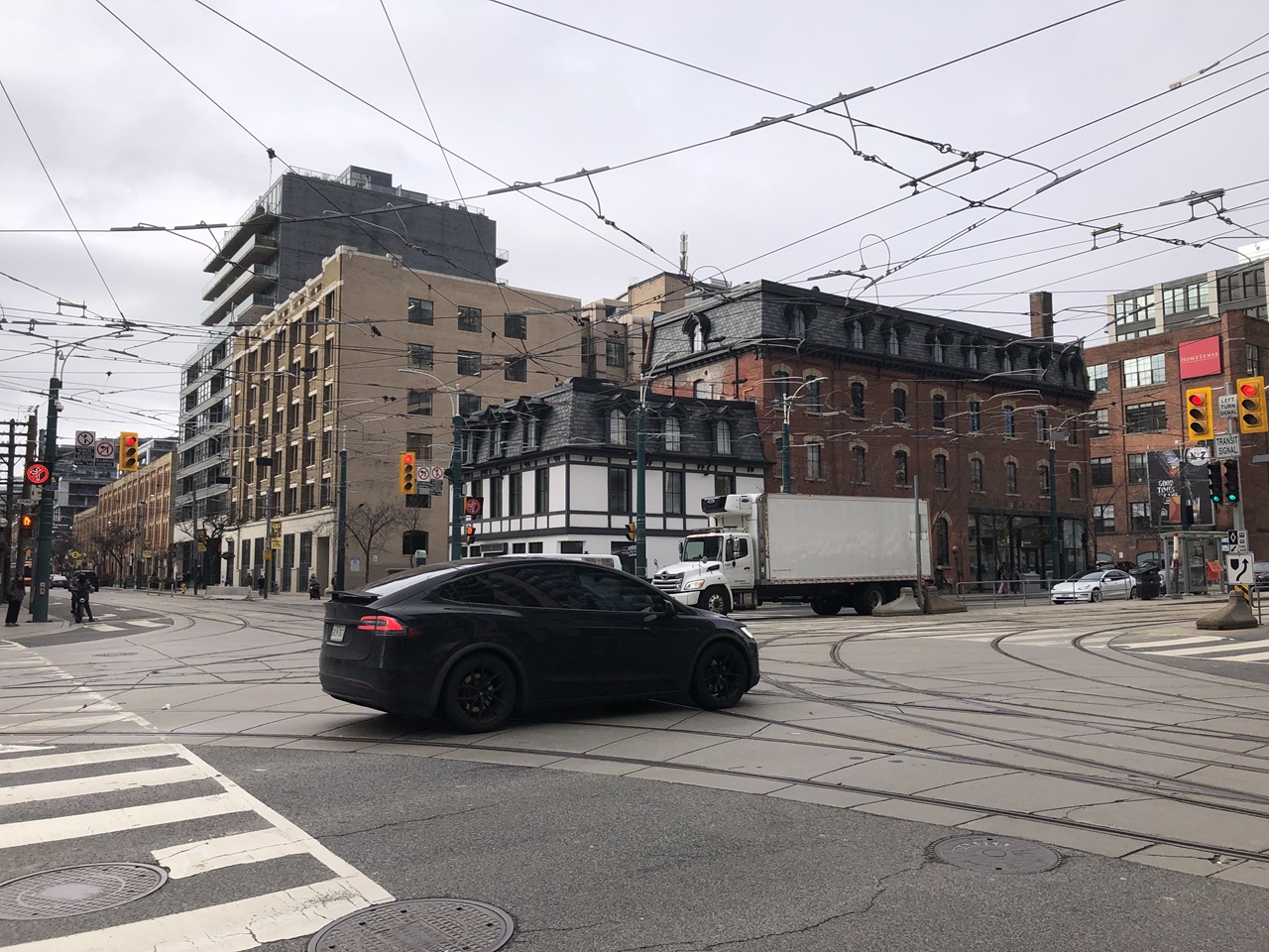 A black SUV navigates a complex downtown intersection with streetcar tracks and overhead transit wires as a white box truck drives in the background, representing traffic safety hazards, rising speeding violations, and car accident personal injury claims in Toronto and the Greater Toronto Area (GTA).